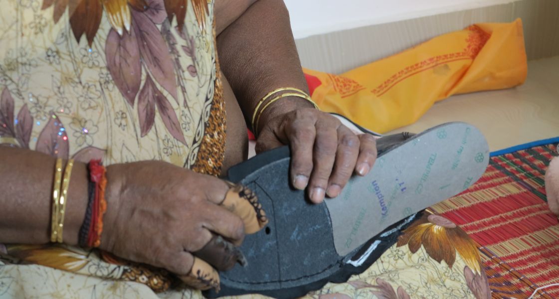 Eine Frau hat einen halbfertigen Schuh in der Hand. Drei Finger einer Hand sind mit einem Lederschutz überzogen.