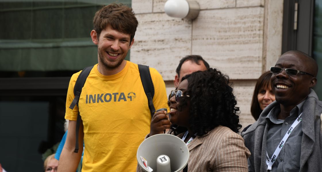 Ein junger Mann mit gelben T-Shirt lächelt eine Frau an, die in ein Megafon sprich