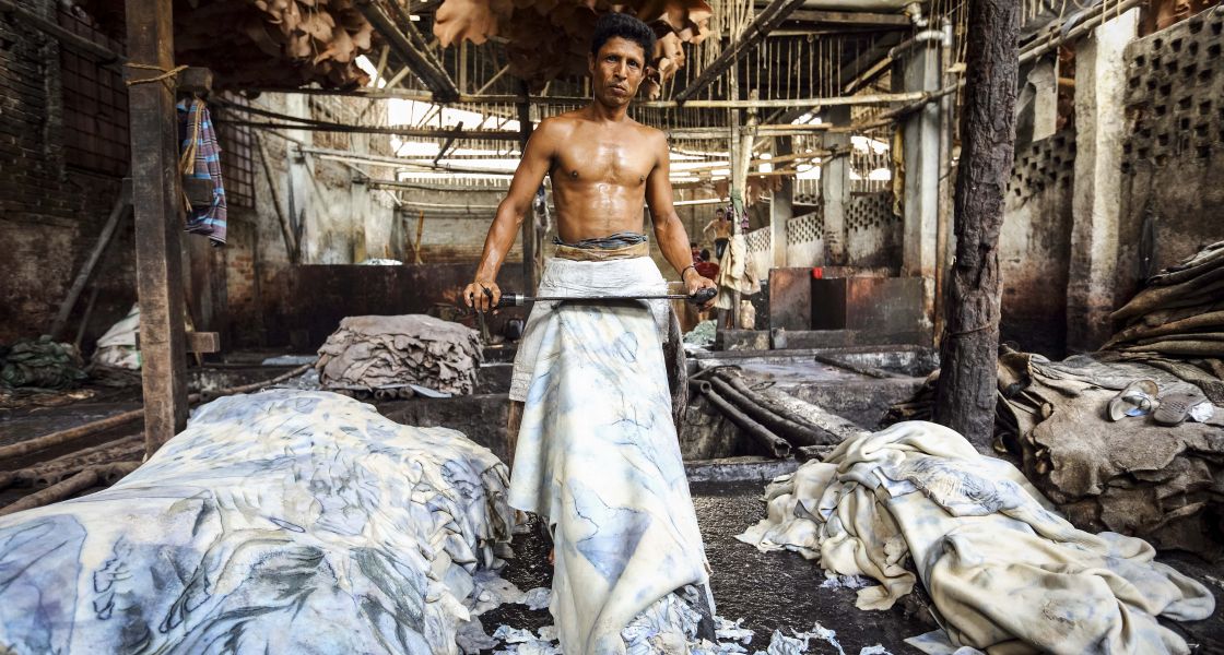 Ein Mann mit freiem Oberkörper gerbt ein großes Stück Leder mit einem großen Messer vor seinem Körper
