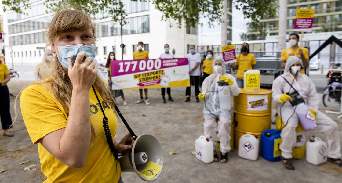 Eine junge Frau mit Maske im Gesicht spricht durch ein Megafon. Sie ist Teil einer Protestgruppe.