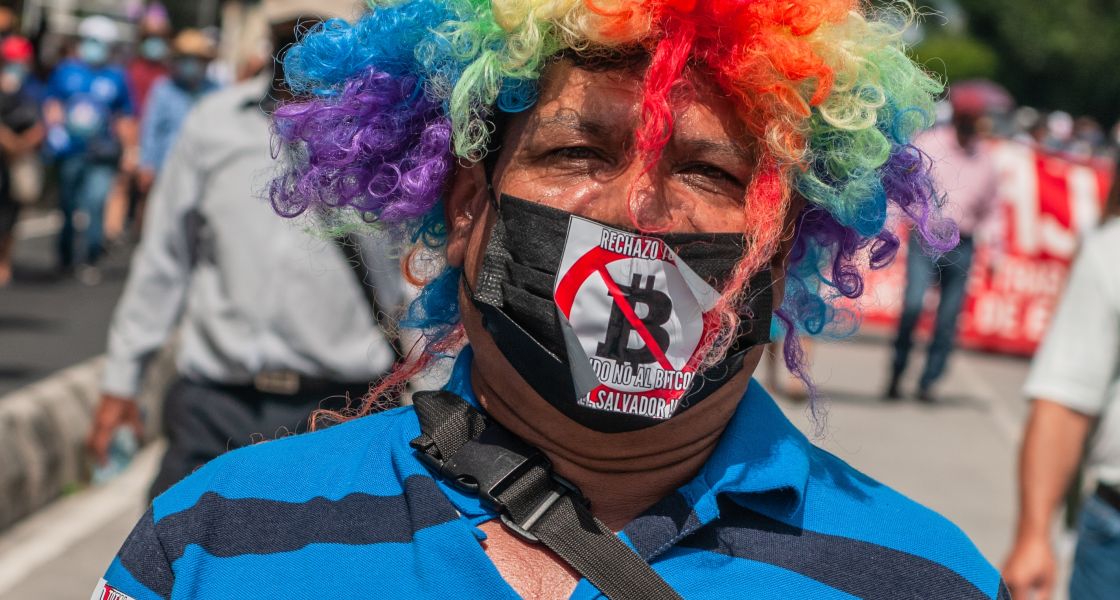 Mann mit Clownsperücke und Protestaufklebern auf seiner Kleidung
