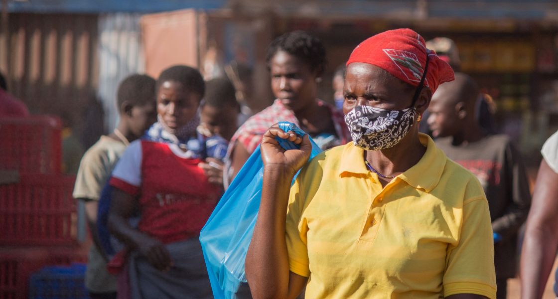 Eine Frau mit Mundschutz und rotem Kopftuch hält ein blaue über der Schulter fest