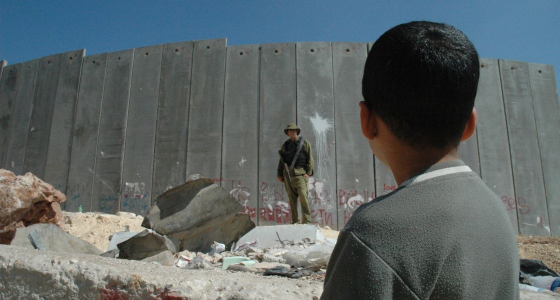 Ein Junge steht vor einer riesigen Mauer, die von einem Soldaten beschützt wird.