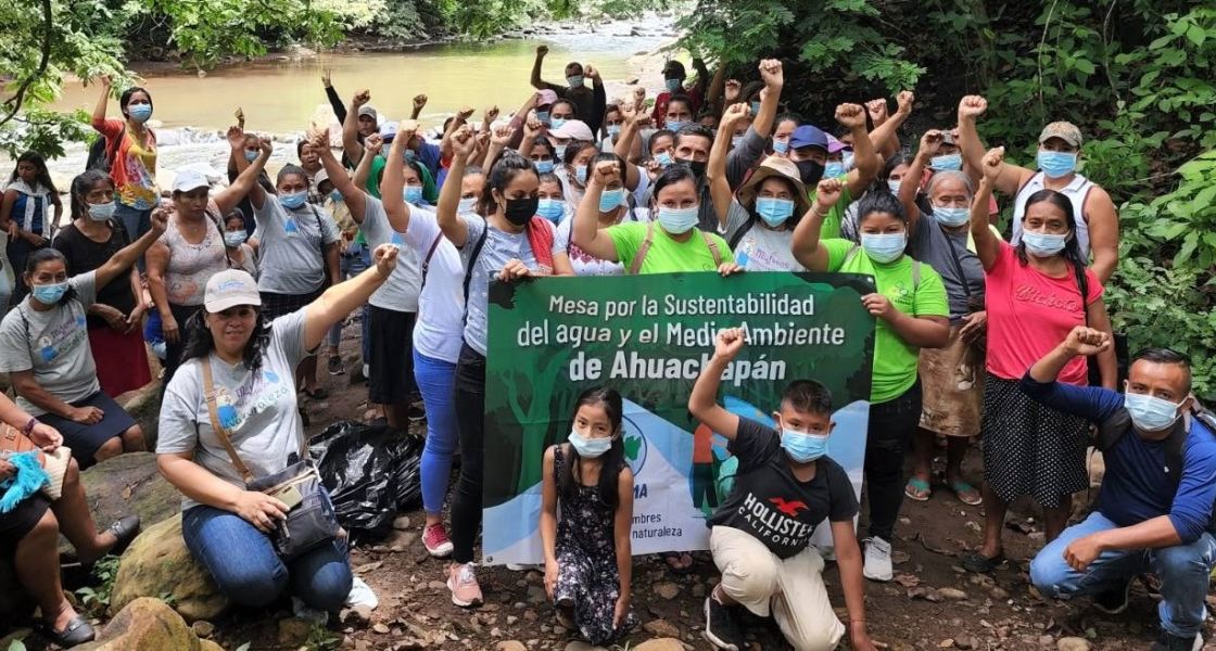 Viele Menschen, die die Fäuste hochheben, und mit einem Banner vor einem Fluss protestieren