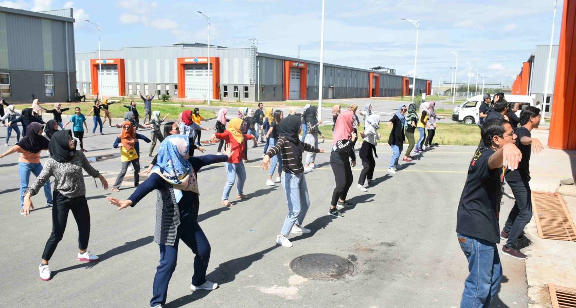 Ein großer Platz, auf dem sich viele Personen sportlich betätigen. Im Hintergrund sind große Fabrikhallen zu sehen.