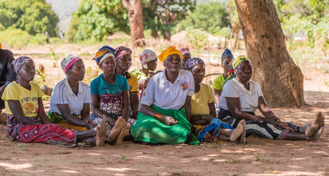 Frauen in bunter Kleidung sitzen auf dem Boden im Schatten eines Baumes