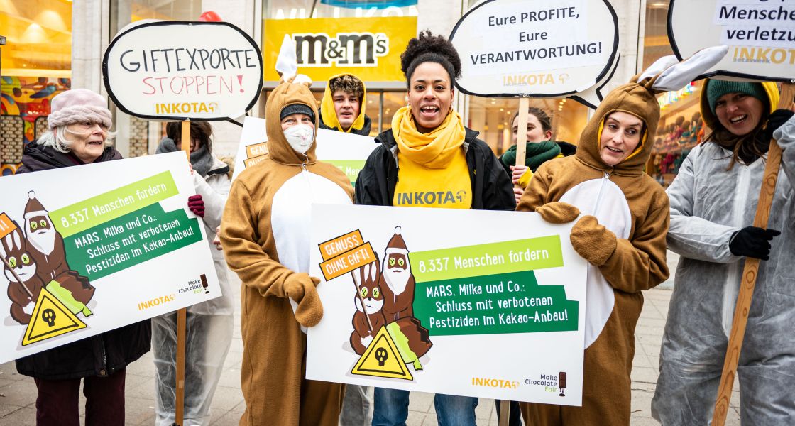Mitarbeiter*nnen von INKOTA protestieren mit Schildern in der Hand vor einem Schokoladengeschäft