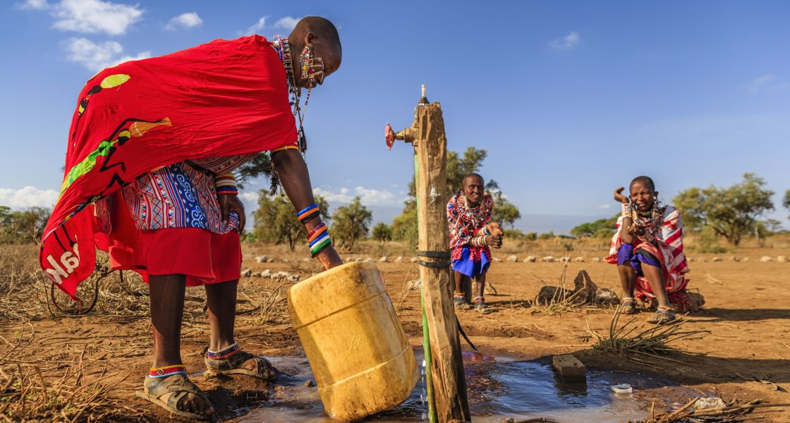 Eine Massai-Frau hebt einen großen Kanister an, der mit Wasser gefüllt ist