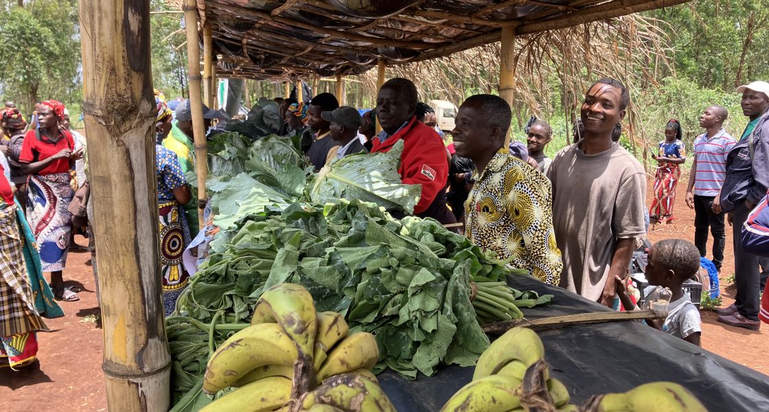 Eine Gruppe Männer und Frauen verkaufen ihr Gemüse an überdachten Ständen.