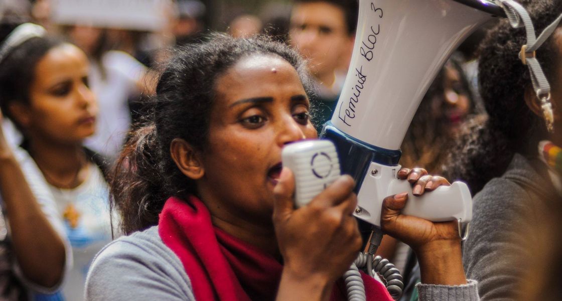 Eine Frau mit rotem Schal und einem Megafon spricht in das Gerät rein