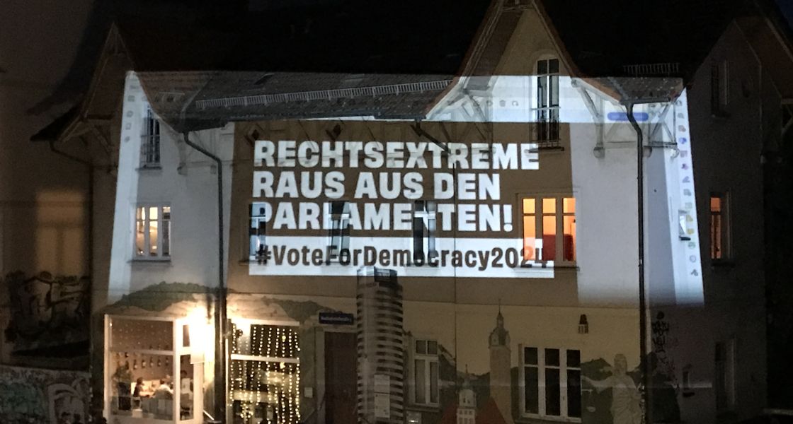 Ein Haus nachts, auf das der Spruch "Rechtsextreme raus den Parlamenten" projiziert wird