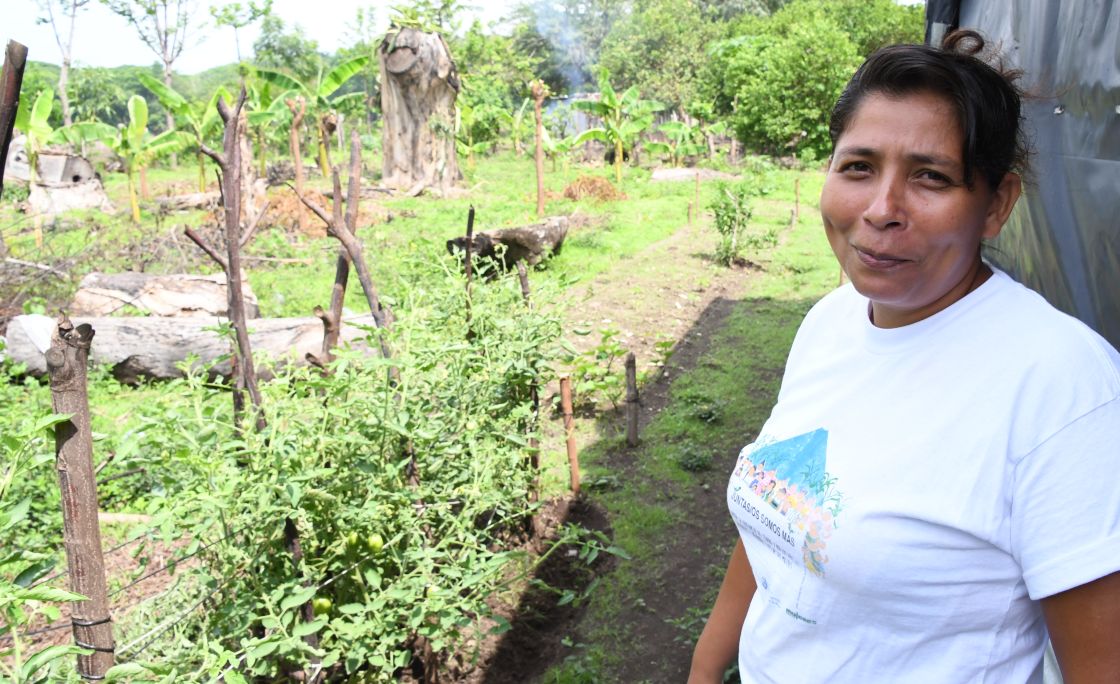 Eine Frau mit weißem T-Shirt steht vor einem Gemüsebeet