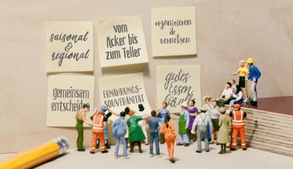 Eine Gruppe Miniaturmenschen stehen vor großen Plakaten