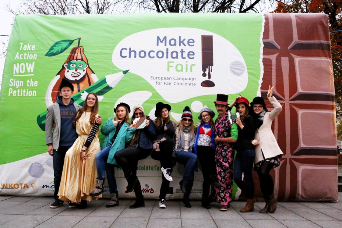 Eine gruppe junger Leute mit Hüten verkleidert posen vor einer übergroßen Tafel Schokolade