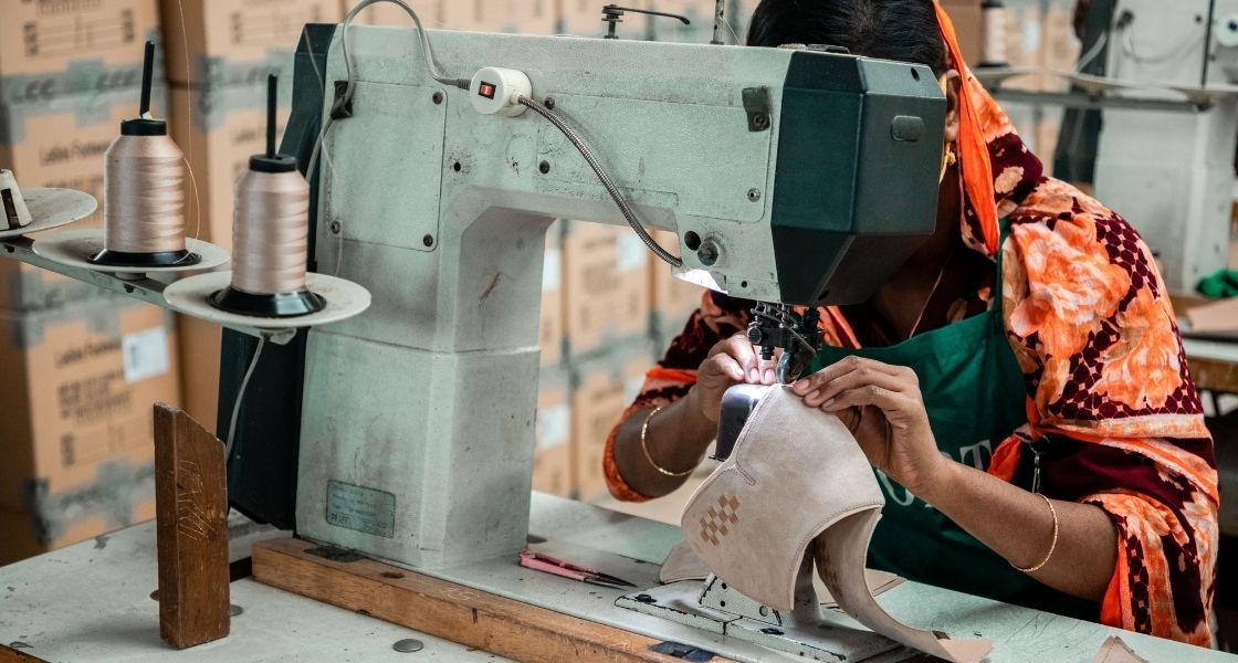 Eine Frau sitzt an einer Nähmaschine und näht Lederteile zusammen