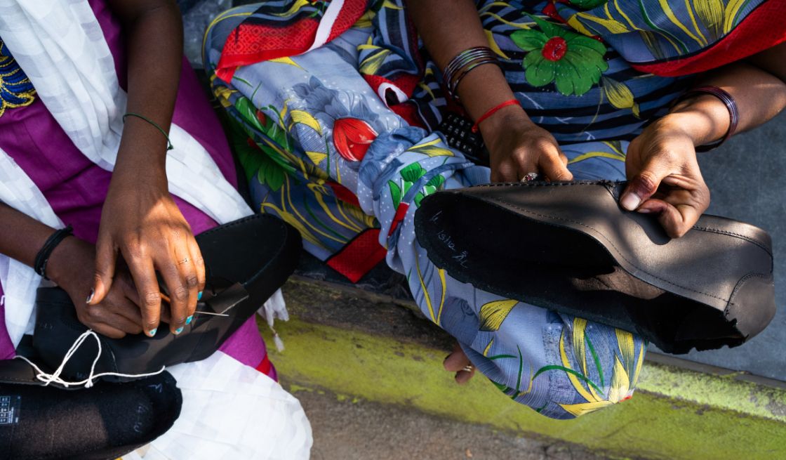 Zwei Frau sitzen nebeneinander und eine Frau näht gerade einen Lederschuh