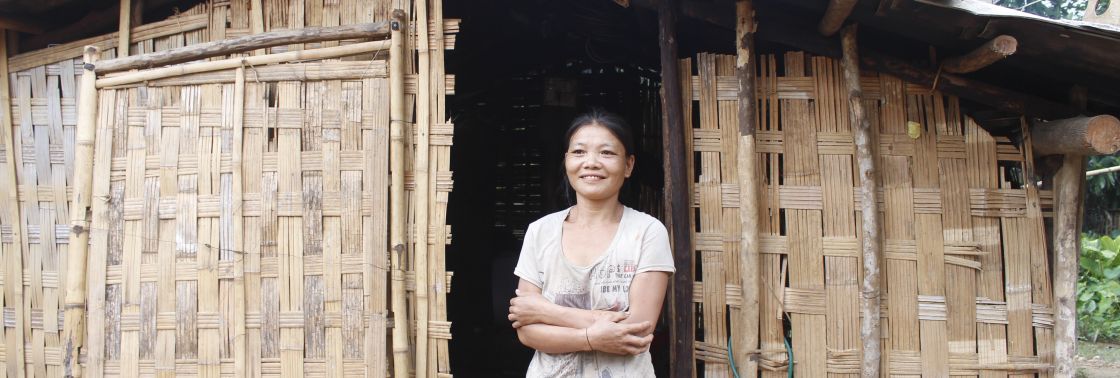 Eine Frau steht mit verschränkten Armen vor einer Bambushütte