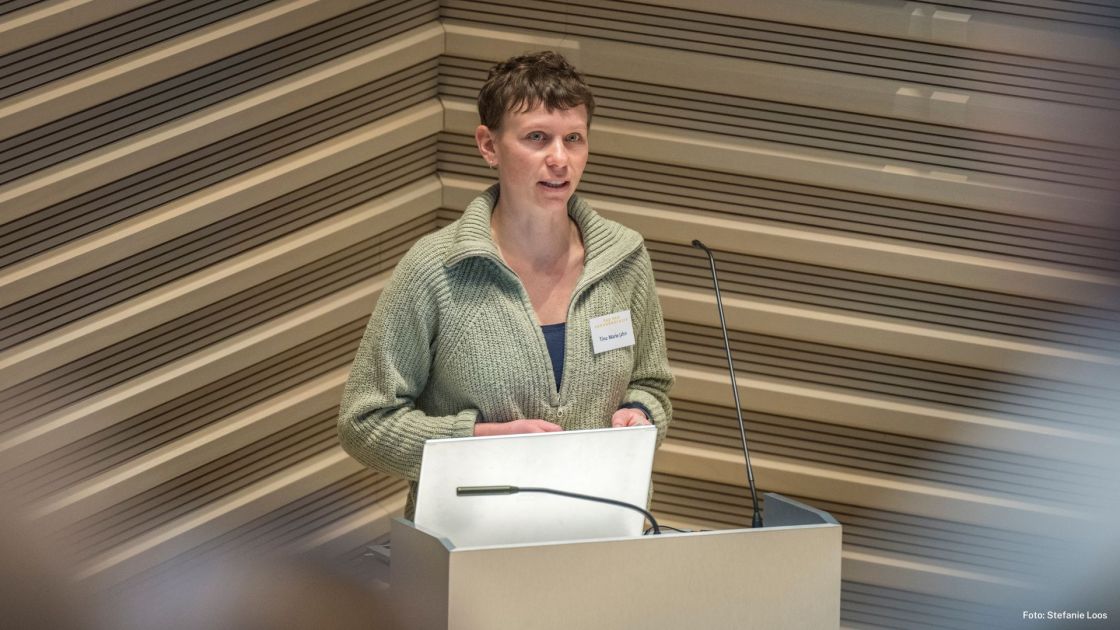 Eine Frau in hellgrünem Pullover steht vor einem Pult mit Mikrofon