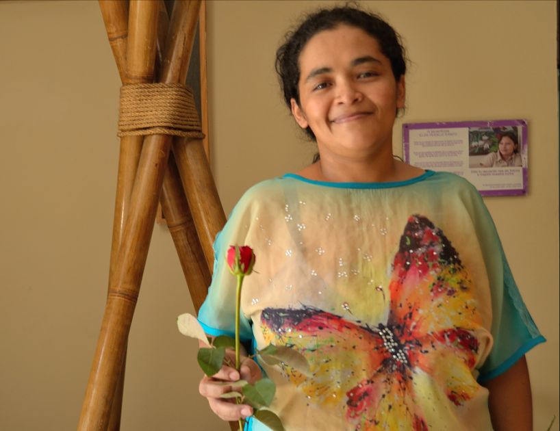 Eine junge Frau mit dunklen Haaren, die in der Hand eine Rose hält und lächelt.