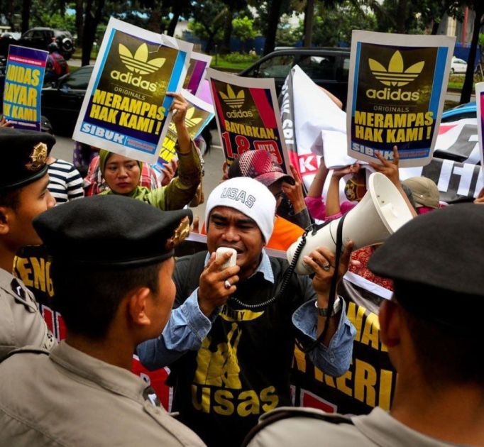 Eine Menschenmenge. Im Zentrum ein Mann spricht in ein Megafon. Davor Polizisten. Dahinter Protestler.