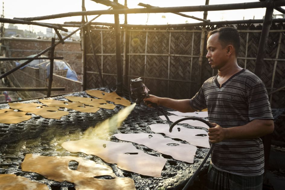 Ein Mann sprüht Lederstücke ein.