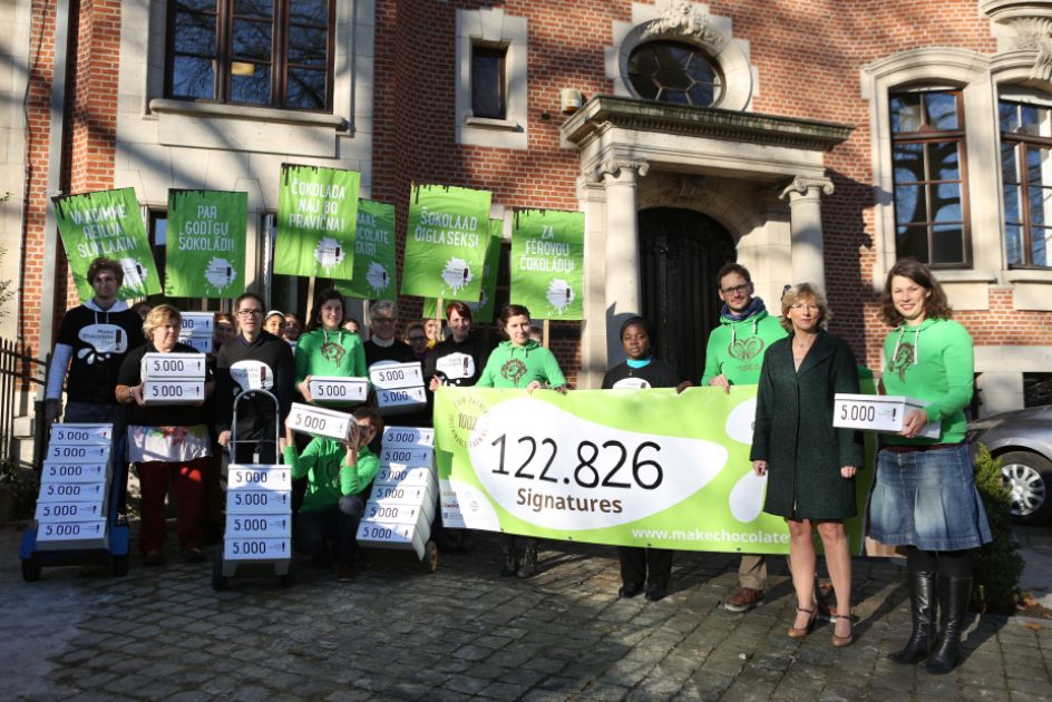 Menschengruppe mit grünen Protestschildern vor einem Bachsteinhaus