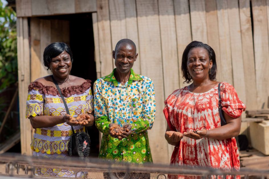 2 Frauen und ein Mann halten Kakaobohne in ihren Händen und lächeln in die Kamera.