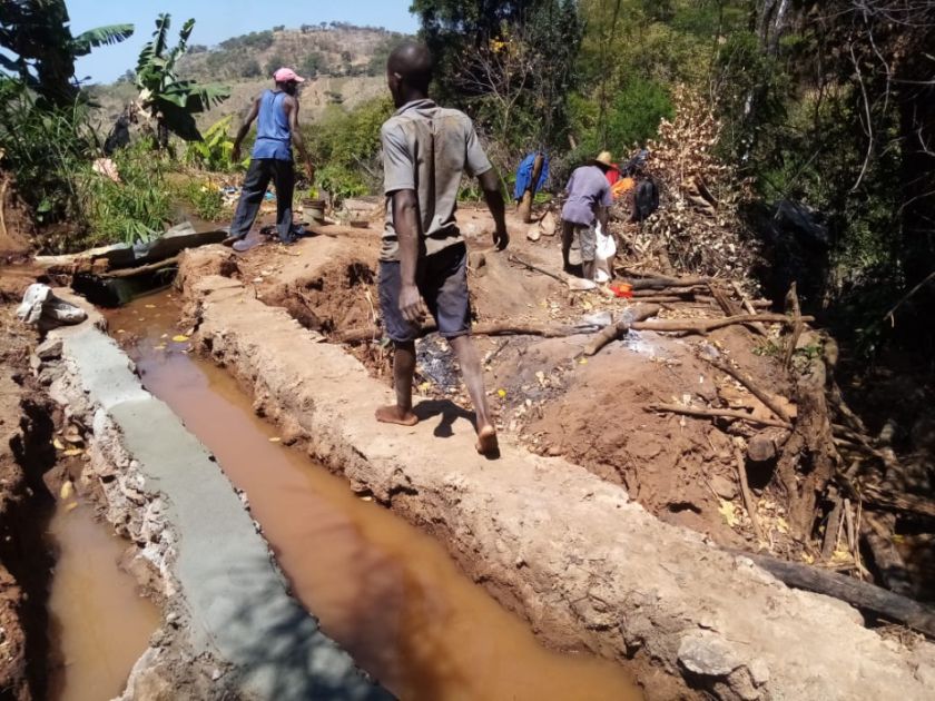 Zwei Männer laufen an einem kleinen Kanal entlang und arbeiten daran