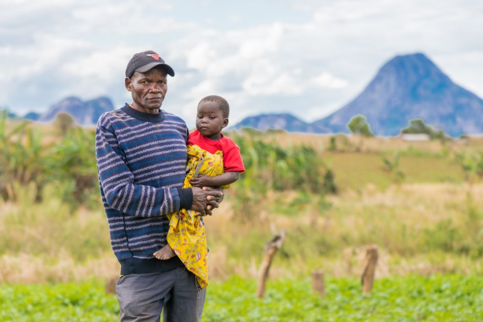 Ein Mann trägt ein Kind. Er steht auf einem Feld
