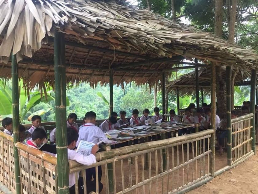 Eine offene Hütte mit einem langen Tisch mit Heften und Büchern, an dem 16 Kinder sitzen