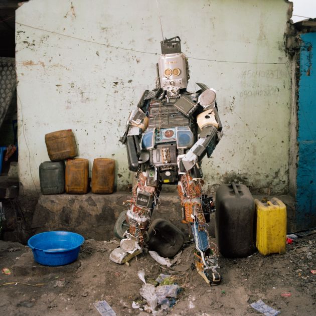 Ein Mann trägt ein Kostum aus alten Radiogeräten, er sieht aus wie ein Roboter. Auch das Gesicht bedeckt.