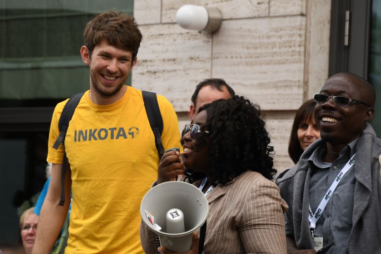 Ein junger Mann mit gelben T-Shirt lächelt eine Frau an, die in ein Megafon sprich