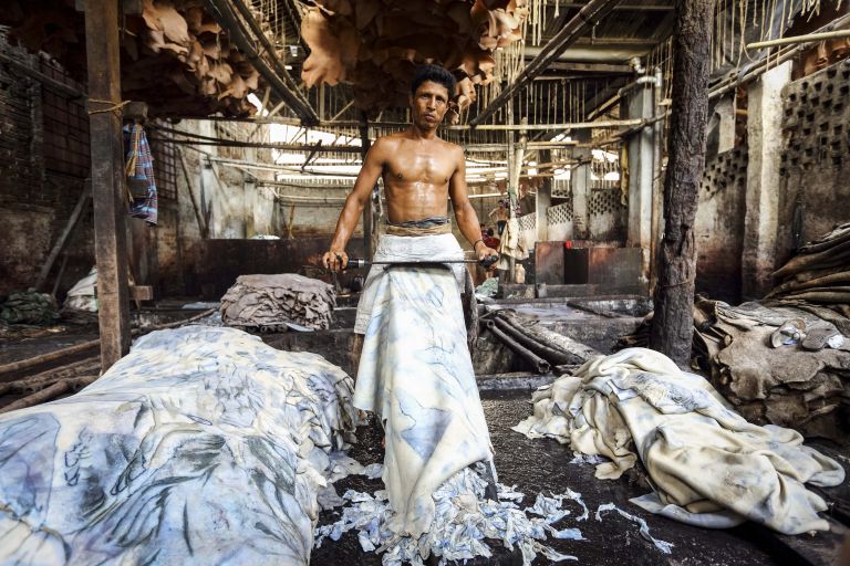 Ein Mann mit freiem Oberkörper gerbt ein großes Stück Leder mit einem großen Messer vor seinem Körper