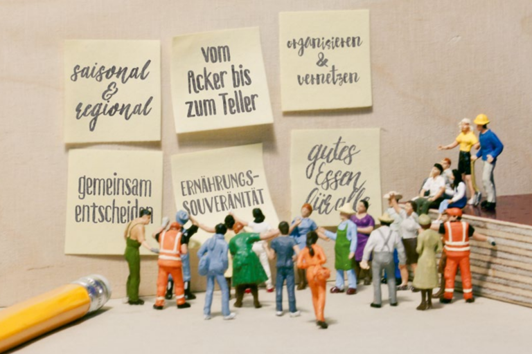 Eine Gruppe Miniaturmenschen stehen vor großen Plakaten