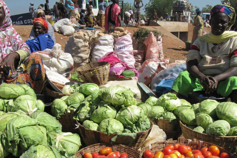 Zwei Frauen sitzen neben mehreren Körben mit Gemüse 