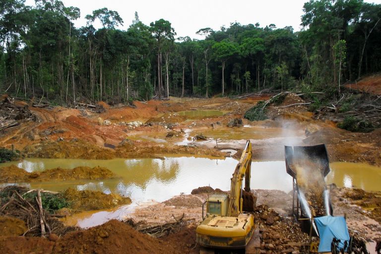 Ein Bagger und eine Maschine stehen an einem Tümpel mitten in einer entholzten Fläche im Tropenwald