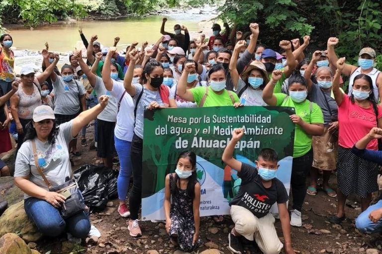 Viele Menschen, die die Fäuste hochheben, und mit einem Banner vor einem Fluss protestieren