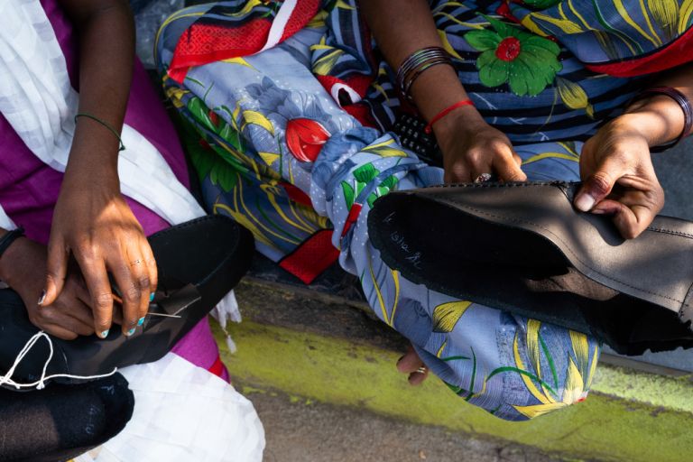 Zwei Frau sitzen nebeneinander und eine Frau näht gerade einen Lederschuh