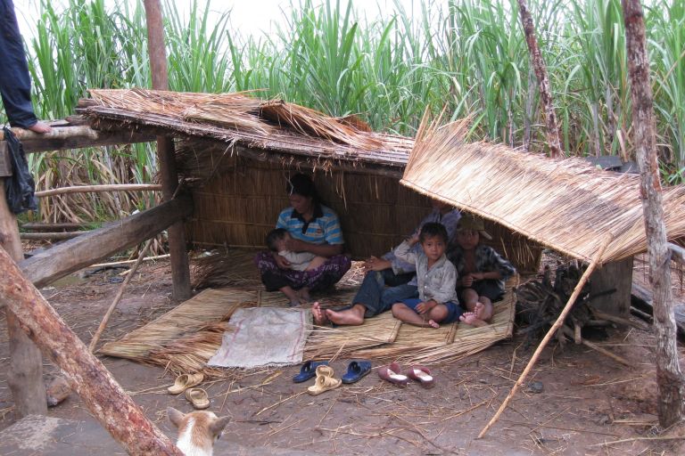 eine Familie mit drei Kindern sitzt unter einem Schilfdach