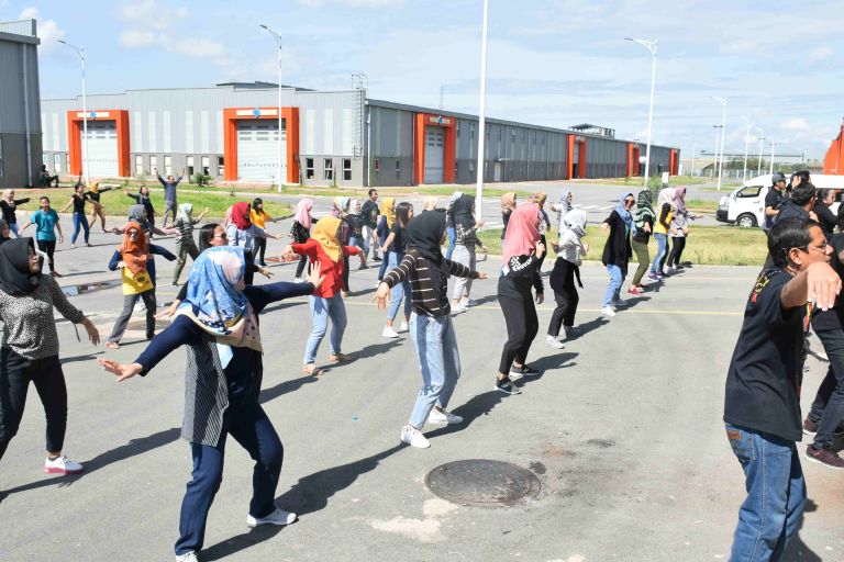 Ein großer Platz, auf dem sich viele Personen sportlich betätigen. Im Hintergrund sind große Fabrikhallen zu sehen.