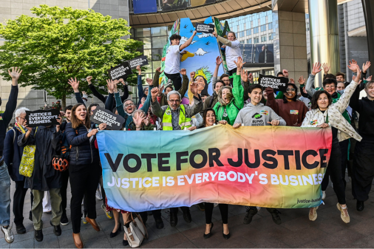 Eine Personengruppe springt in die Höhe und hält dabei ein Banner mit der Aufschrift "Vote for Justice" in die Höhe