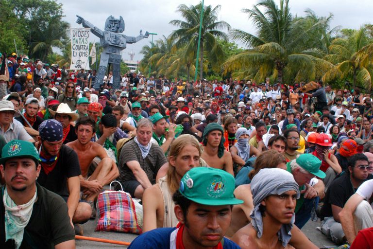 Viele Menschen sitzen auf der Straße. Im Hintergrund stehen Palmen. 