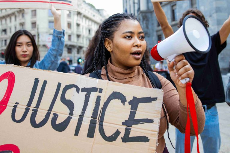 Eine Frau mit Megafon und Protestschild auf der Straße mit anderen zusammen