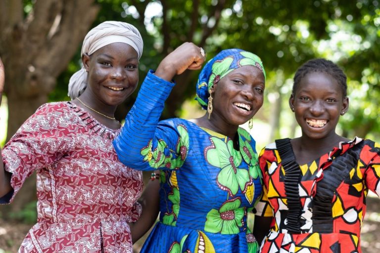 Drei Frauen stehen zusammen und halten je eine Faust hoch und lachen