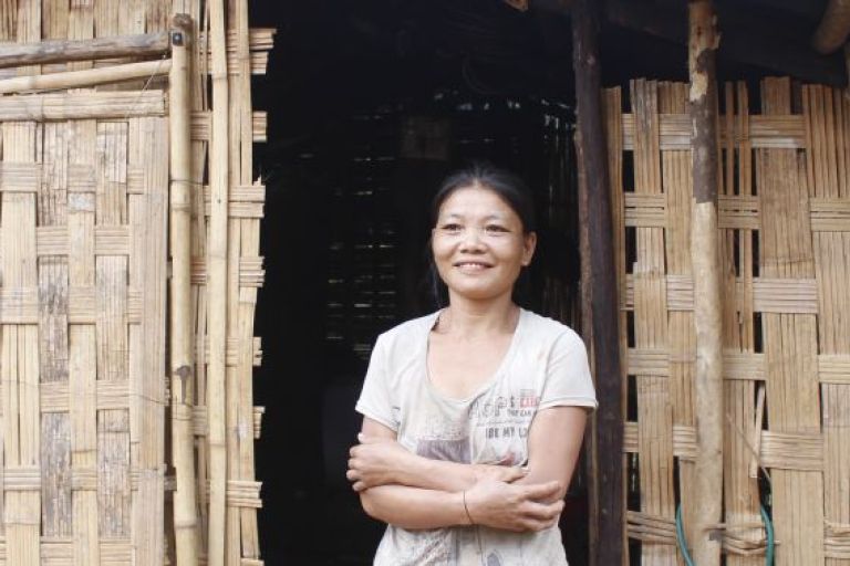 Eine Frau steht mit verschränkten Armen vor einer Bambushütte