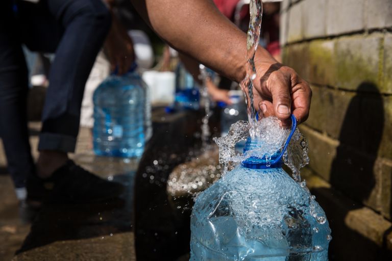 eine große Plastikflasche mit wird Wasser aus einem Hahn gefüllt