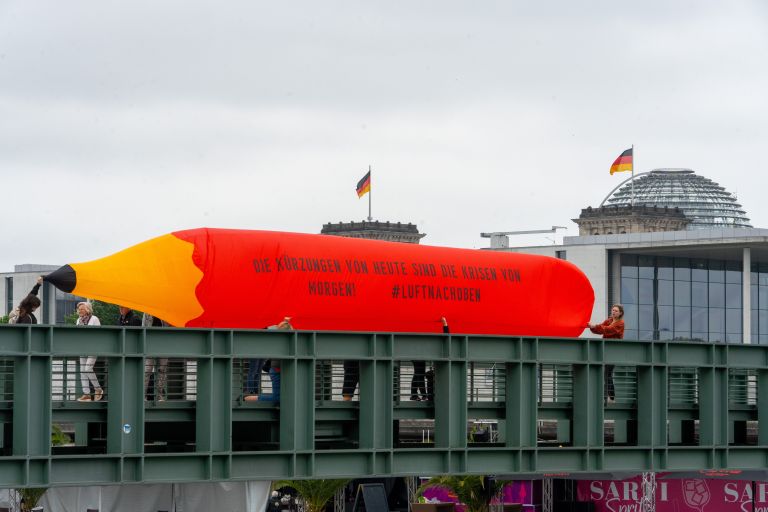 Ein mit Luft gefüllter übergroßer Bleistift wird von Protestlern über eine Brücke im Regierungsviertel Berlins getragen