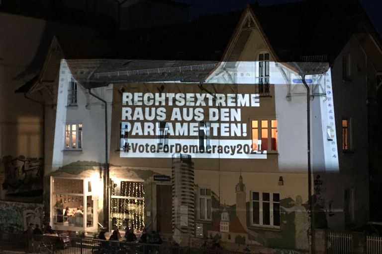 Ein Haus nachts, auf das der Spruch "Rechtsextreme raus den Parlamenten" projiziert wird