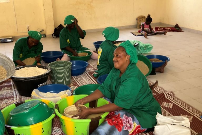 Mehrere Frauen sitzen mit Schüsseln und Mehl auf dem Boden