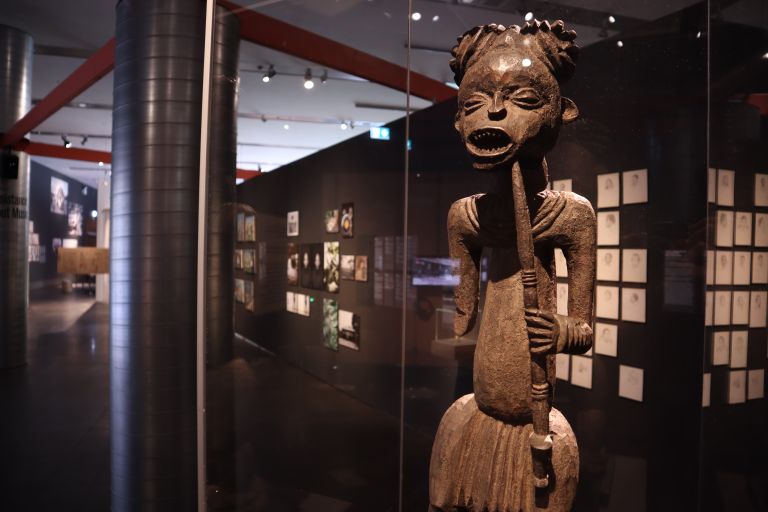 geschnitzte Holzfigur mit ausdruckstarkem Gesicht hinter einer Glasvitrine